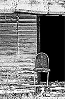 A lone old rickety chair in front of an old cabin with a black darkened doorway