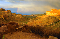 golden sunset with a rainbow between two mountains in the southwest desert