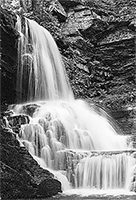 Water falling over a rock cliff with a small body of water beneath