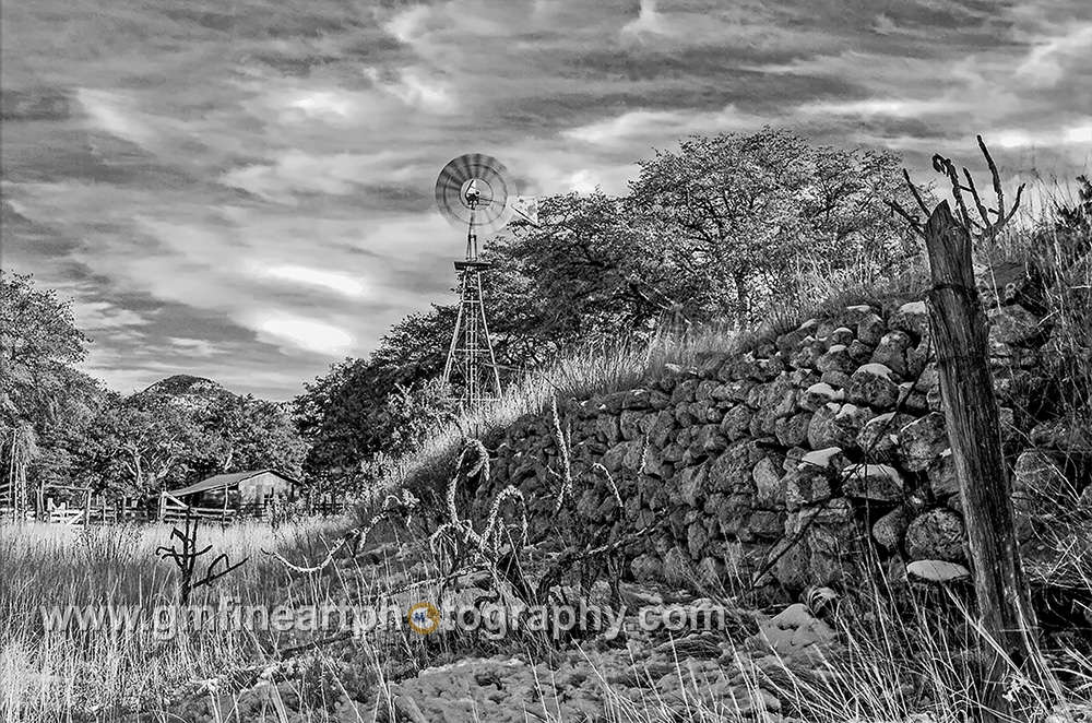 a rock wall leading to an old wind mill water pump on a rustic farm in arizona