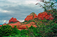 Green trees in front of three red mountain peaks with blue sky
